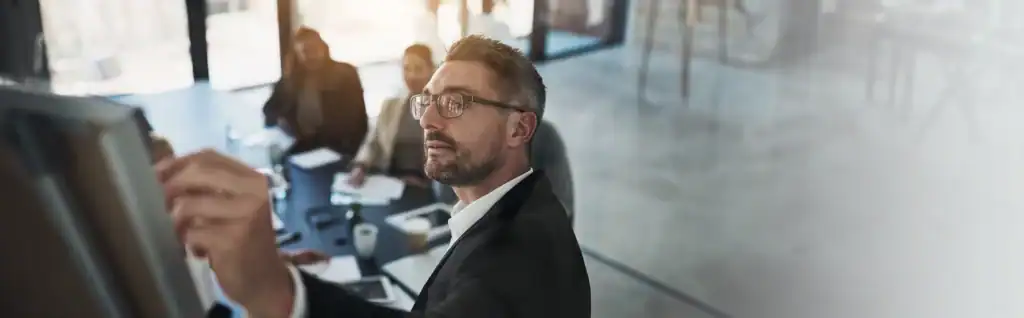 Businessman writing on whiteboard during corporate meeting with team.