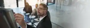 Businessman writing on whiteboard during corporate meeting with team.
