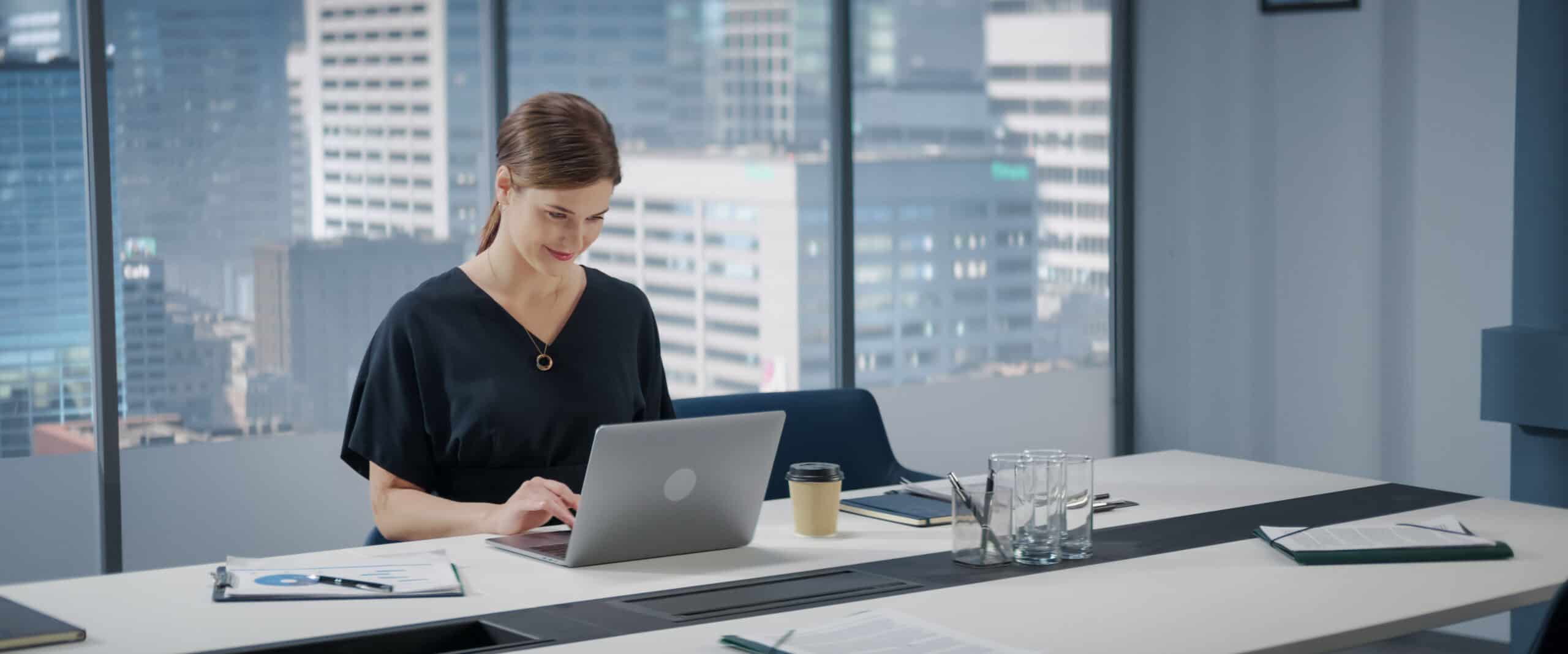 Professional woman working on a laptop in a modern corporate office overlooking the city skyline